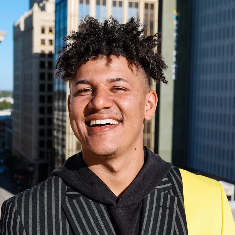 Evan Dougoud, laughing in a pinstriped jacket on a rooftop above downtown Tulsa